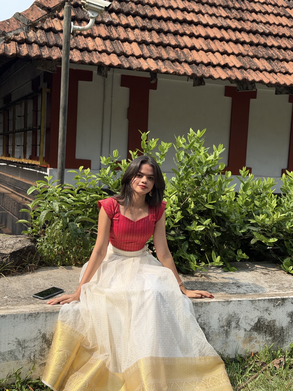 Punnya sitting outdoors in a red blouse and white and gold skirt